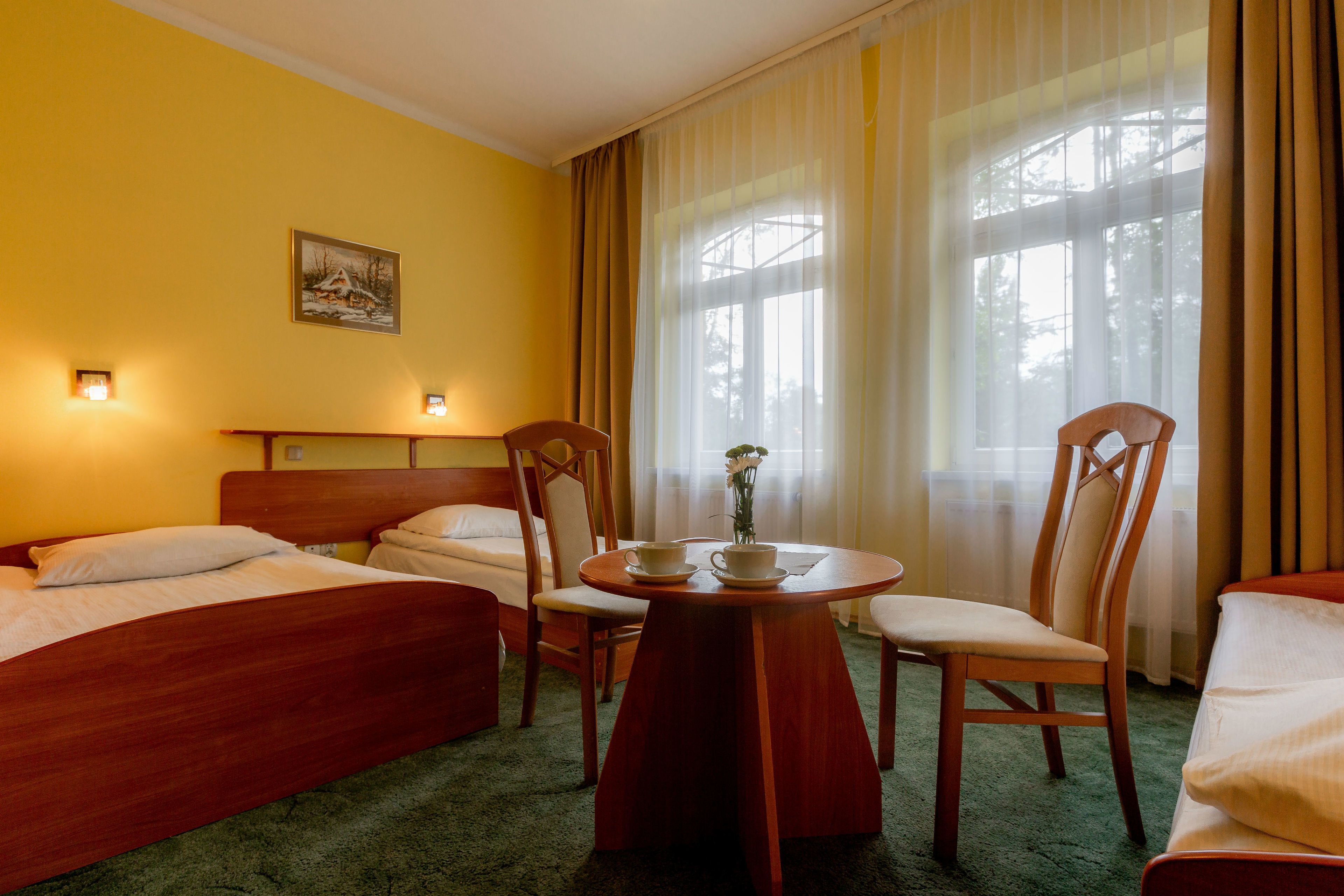 Una habitación de hotel con dos camas, una mesa de comedor con sillas y un cuadro en la pared.