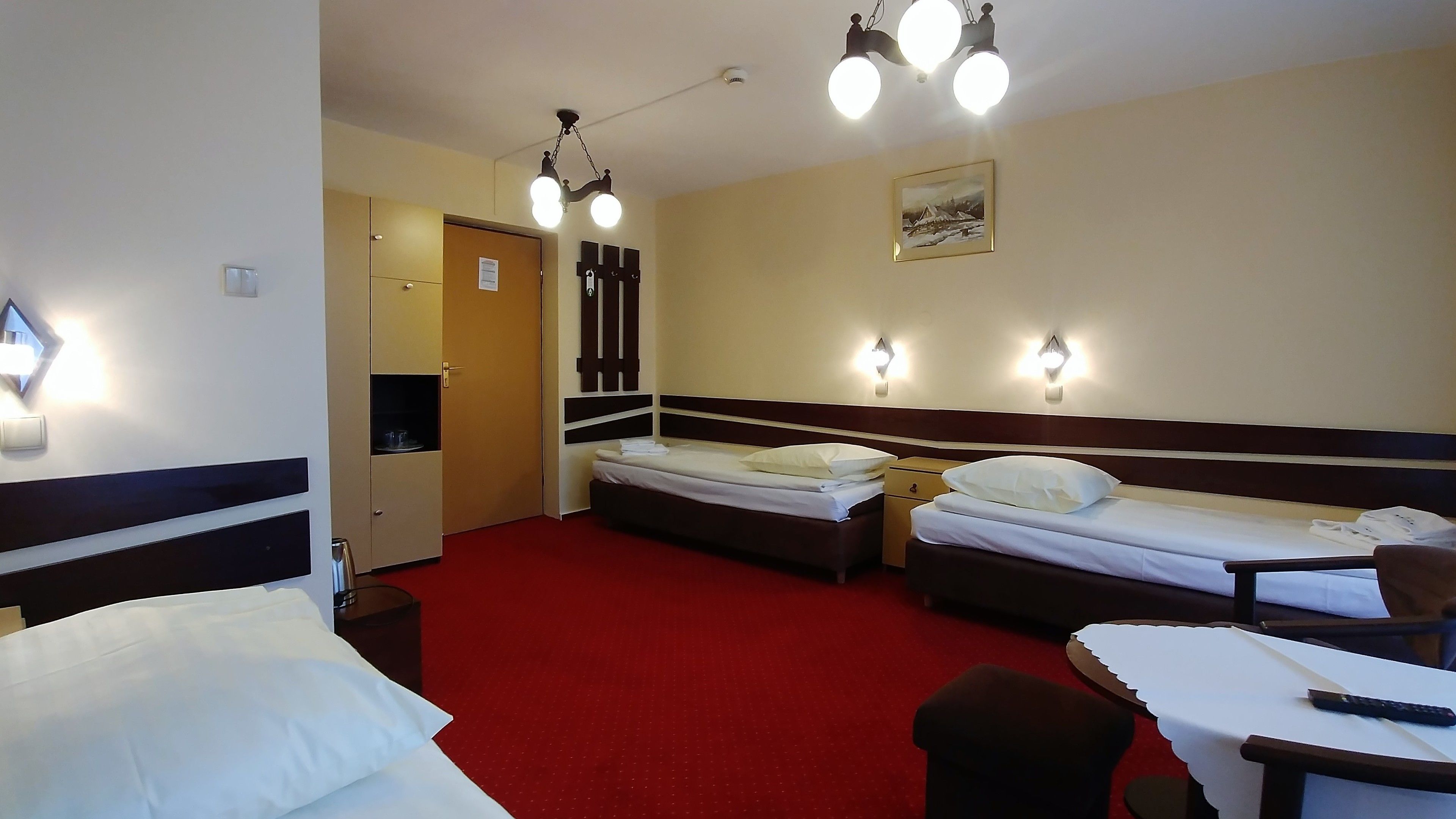 A hotel room with two beds, a desk, and a chair. There are wall-mounted lights and a painting on the wall.