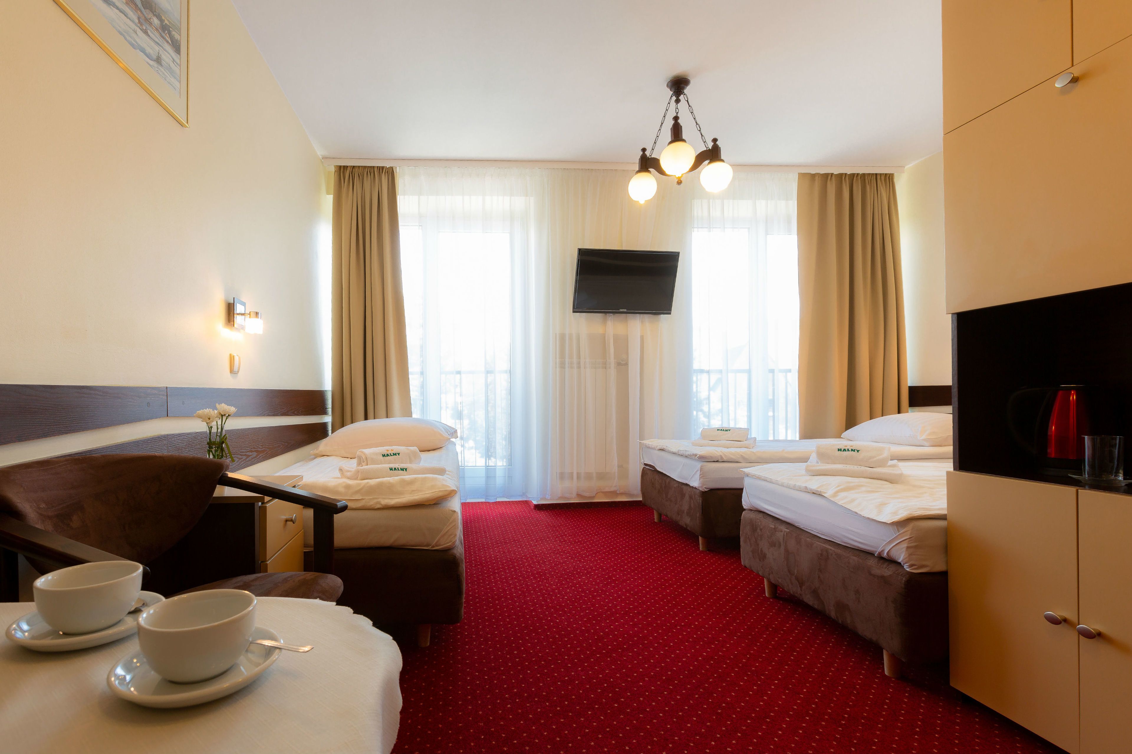 A hotel room with two beds, a TV, a desk with a chair, and a red carpet.