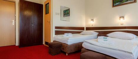 A hotel room with two beds, a red carpet, a wooden wardrobe, a painting, and wall sconces.