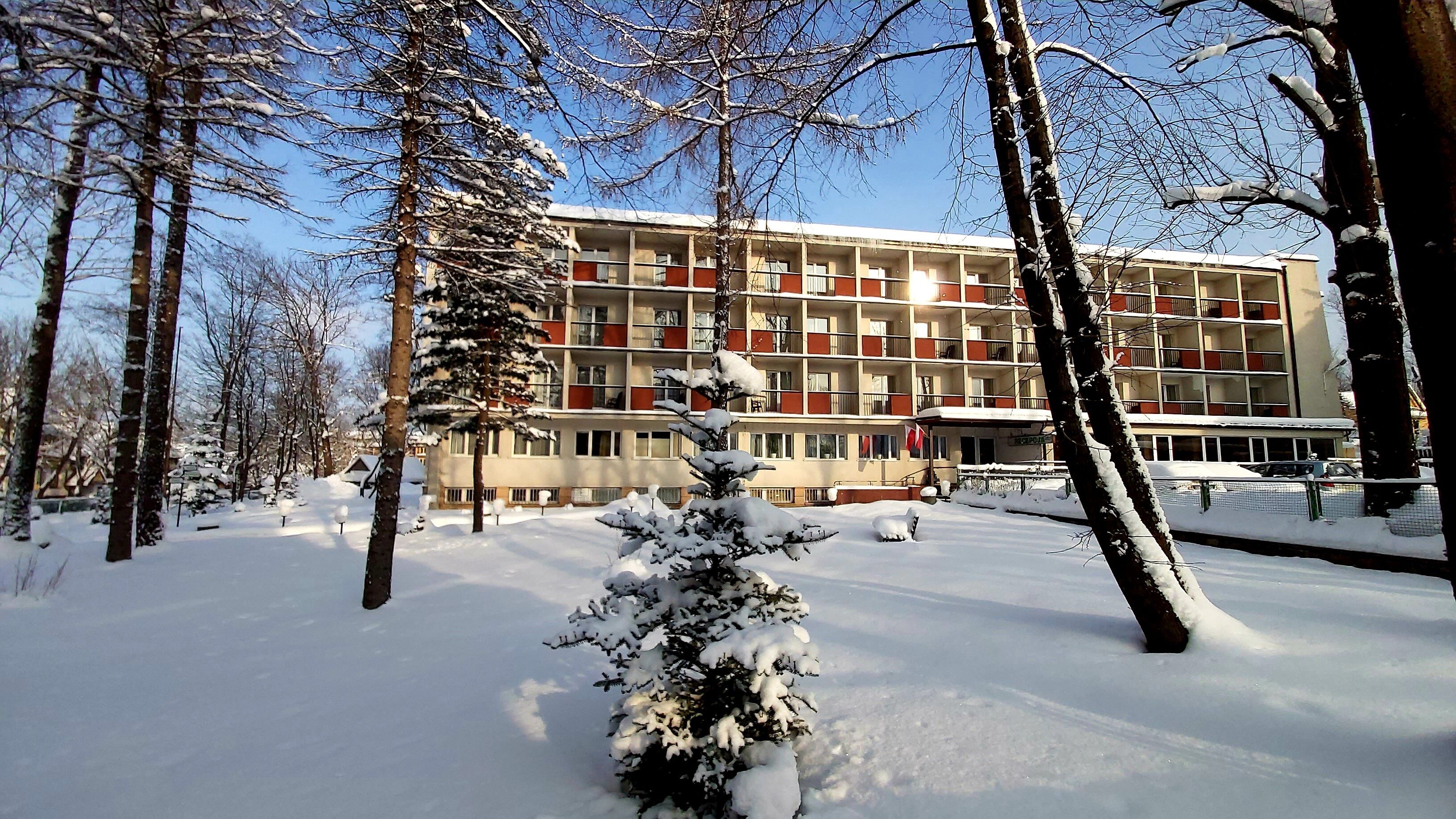 Un edificio de varios pisos con fachada simétrica, rodeado de árboles cubiertos de nieve.
