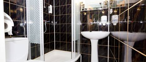 Un baño moderno con ducha envuelta en vidrio, inodoro blanco y lavamanos pedestal.