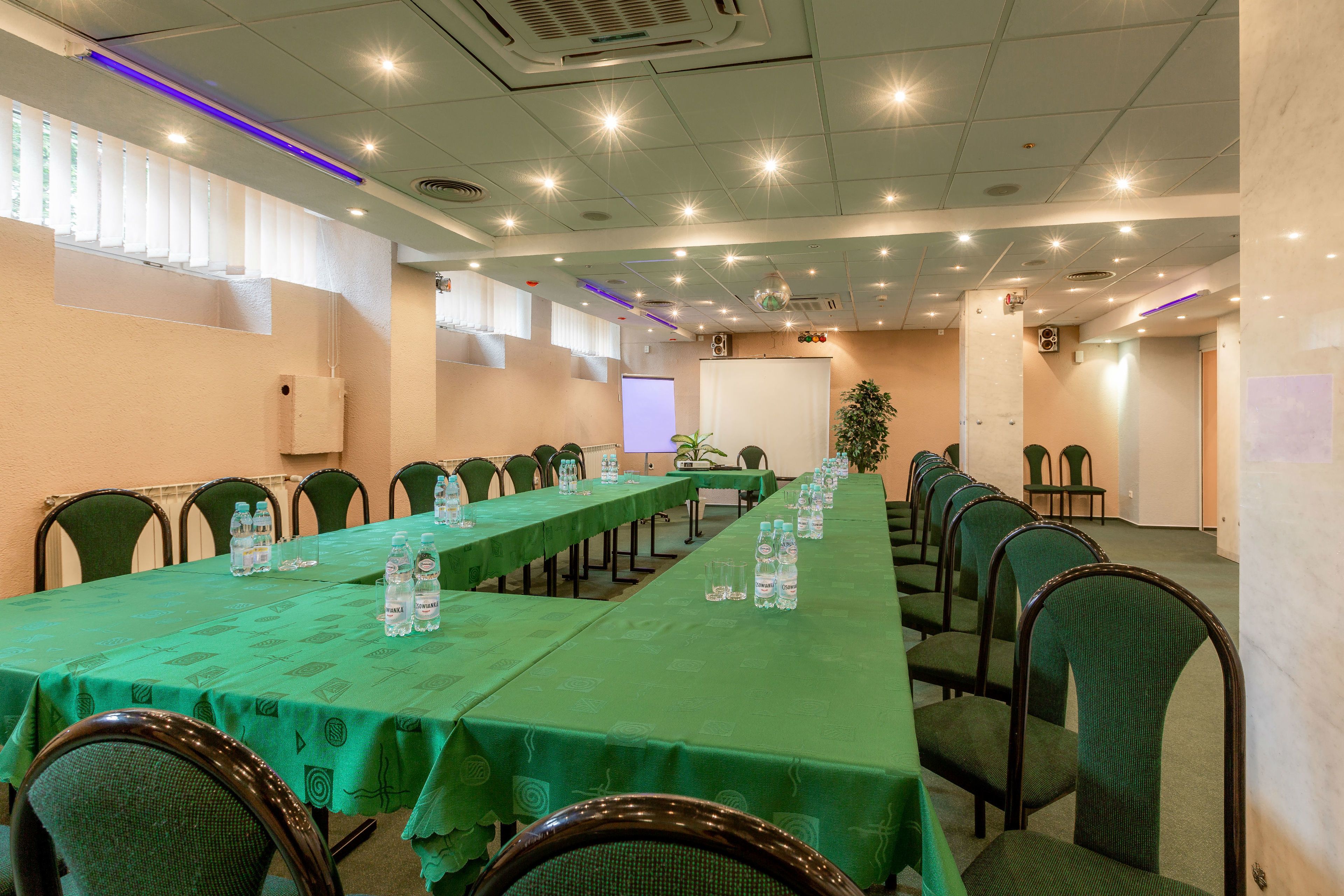 Une salle de conférence avec de longues tables, des chaises et des bouteilles d’eau.