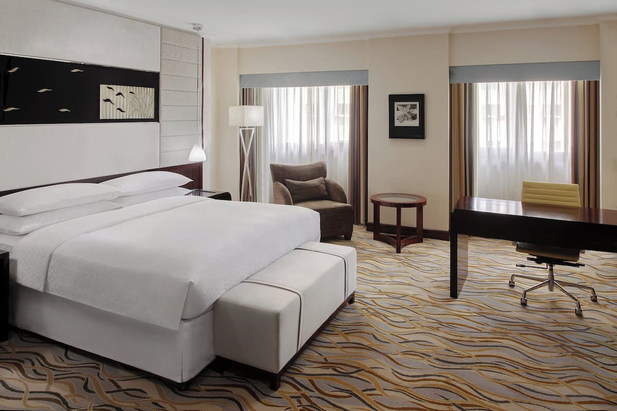 A hotel room with a large bed, a desk, a chair, and a small table.