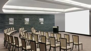 A conference room with rows of chairs, a large screen, and a dark textured wall with framed pictures.