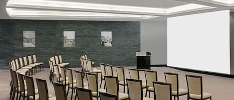 A conference room with rows of chairs, a large screen, and a dark textured wall with framed pictures.