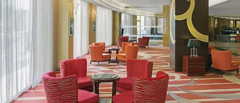 A lobby with red upholstered chairs, a patterned carpet, and a large pillar with a gold design.