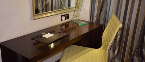 A hotel room with a dark wooden desk, a mirror, a yellow chair, and striped curtains.