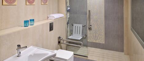 Un baño moderno con un lavamanos blanco, cabina de ducha con vidrio y detalles decorativos en la pared.