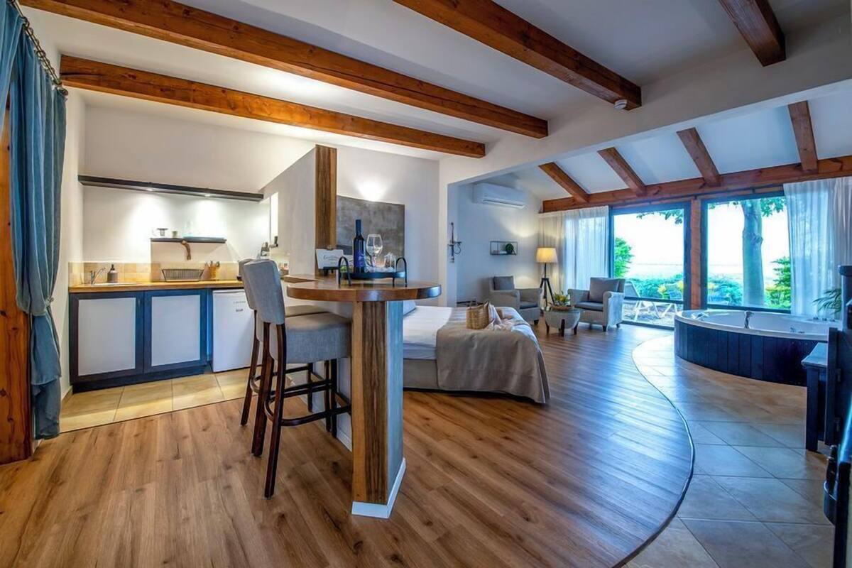 Een ruime woonkamer met een keuken, houten balken, een eettafel en een groot raam met uitzicht.