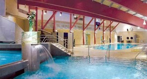 An indoor swimming pool with a waterfall feature, a statue, and a red ceiling structure. - Hotel Centurio (Neustadt an der Donau)