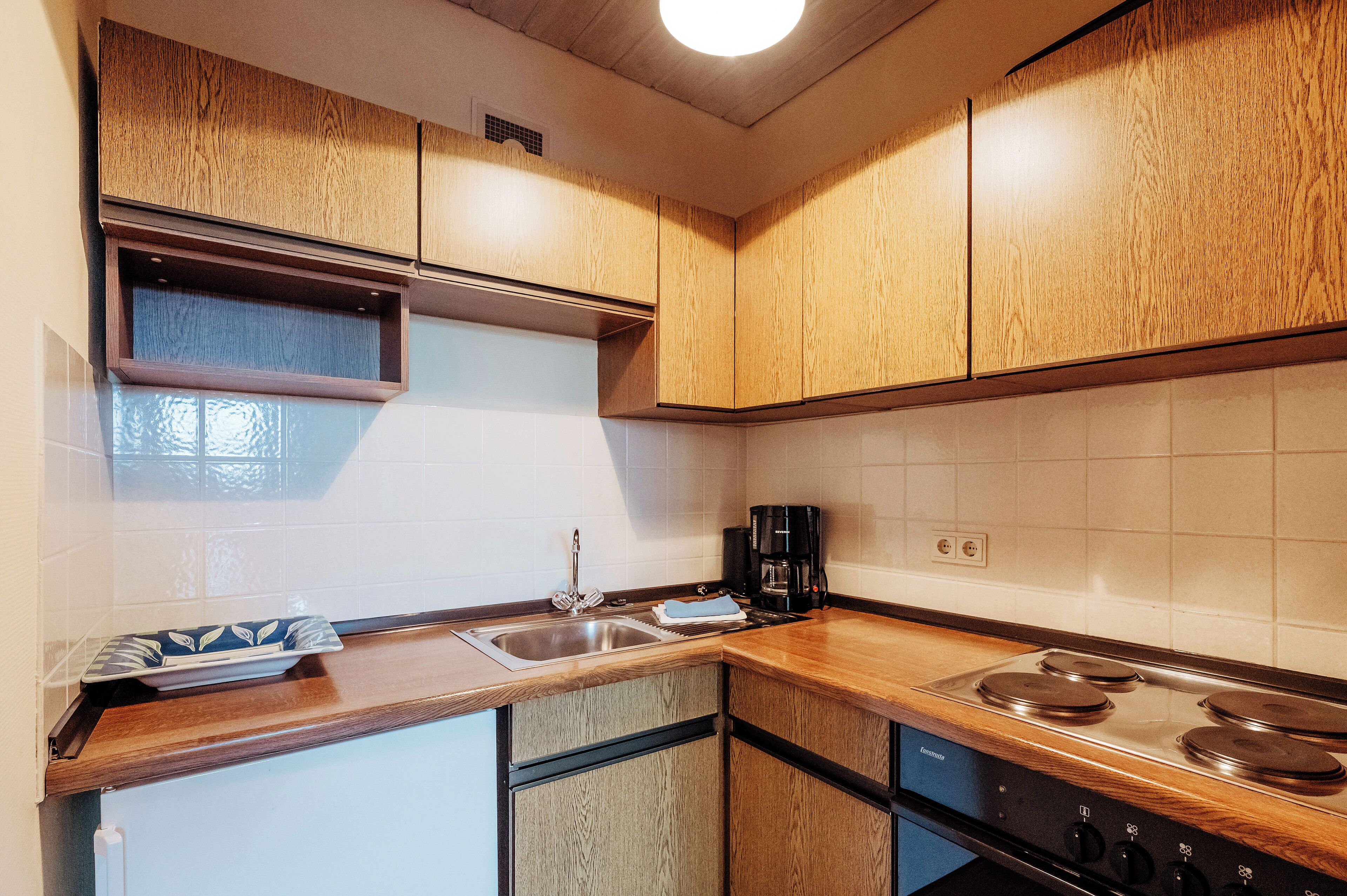 A kitchen with wooden cabinets, a stainless steel sink, a stove, and a coffee maker.