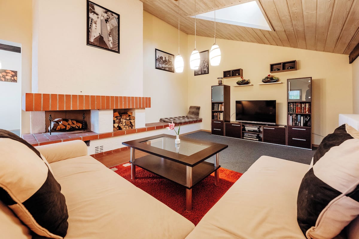 A modern living room with a glass coffee table, a fireplace, a TV, and a bookshelf.