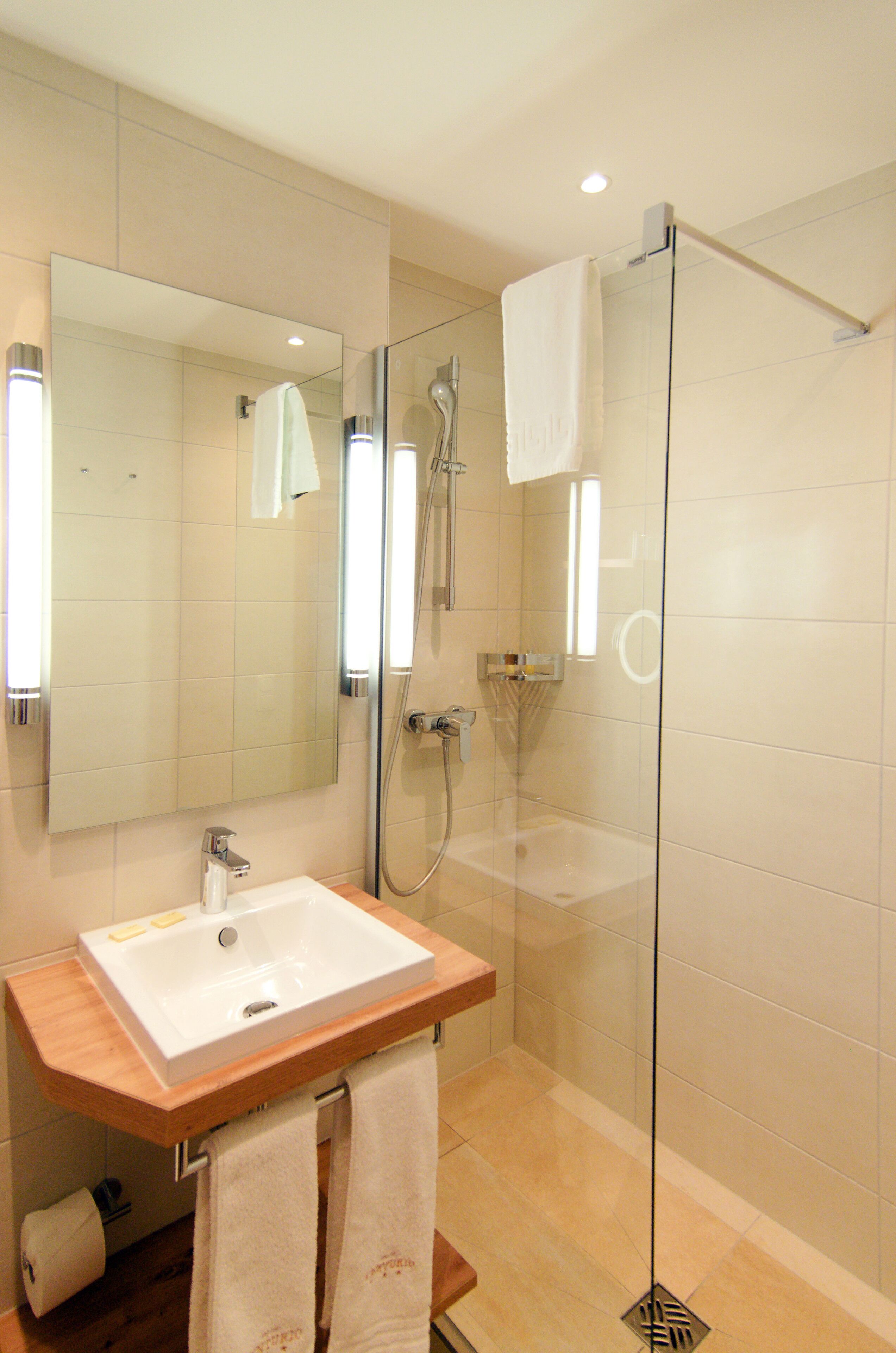A modern bathroom with a glass-enclosed shower, a wooden vanity with a sink, and a large mirror.