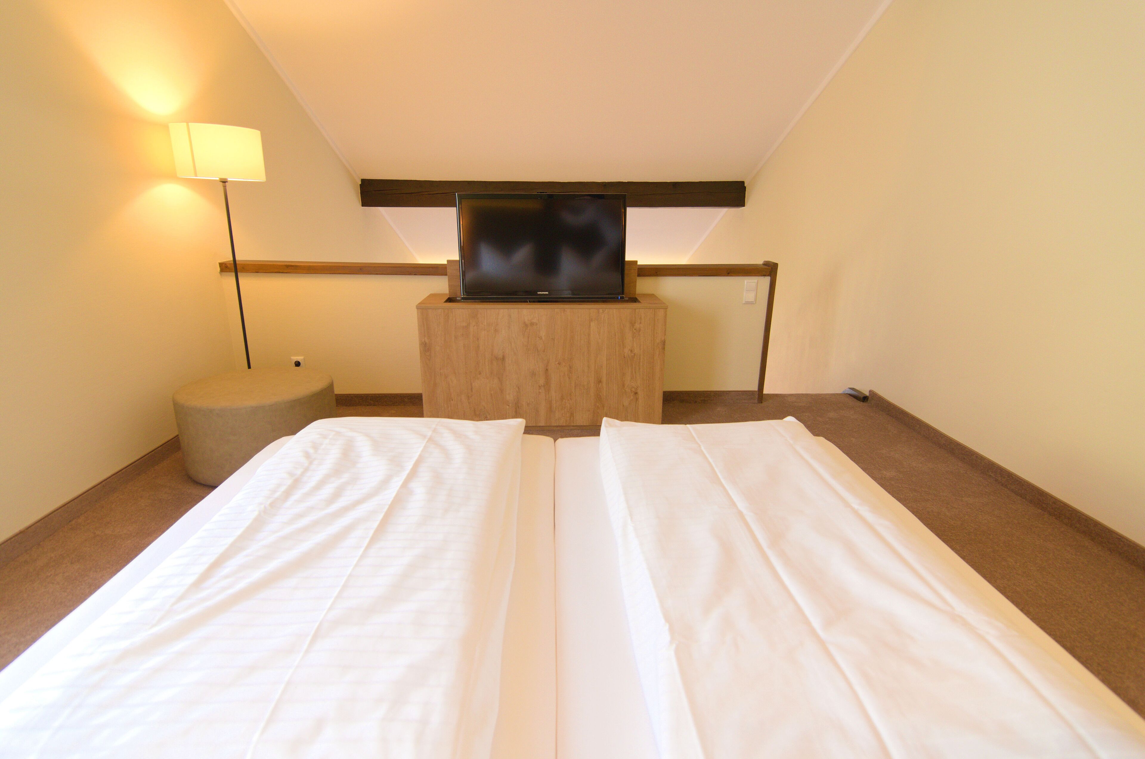 A hotel room with a bed, a TV on a wooden stand, a lamp, and a small stool.