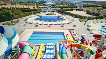 A water park with a pool, slides, and a view of the sea and buildings in the background.