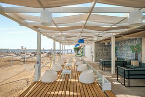 A covered outdoor seating area with wooden flooring and white cushioned seating, overlooking a beach. - Mövenpick Waterpark Resort & Spa Soma Bay (Soma Bay)