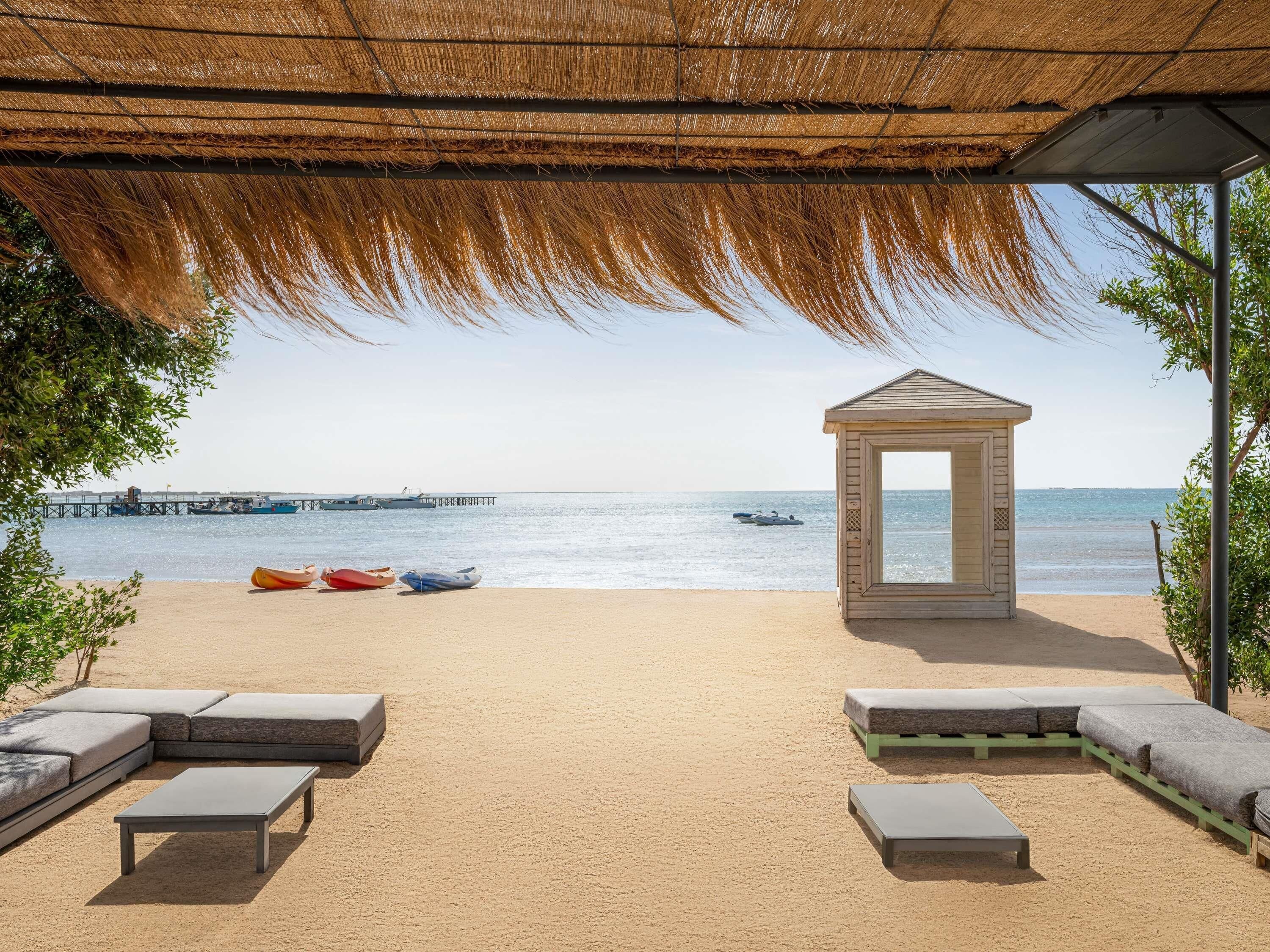 Un salón junto a la playa con techo de paja, un pabellón y zonas de estar con vistas al mar.