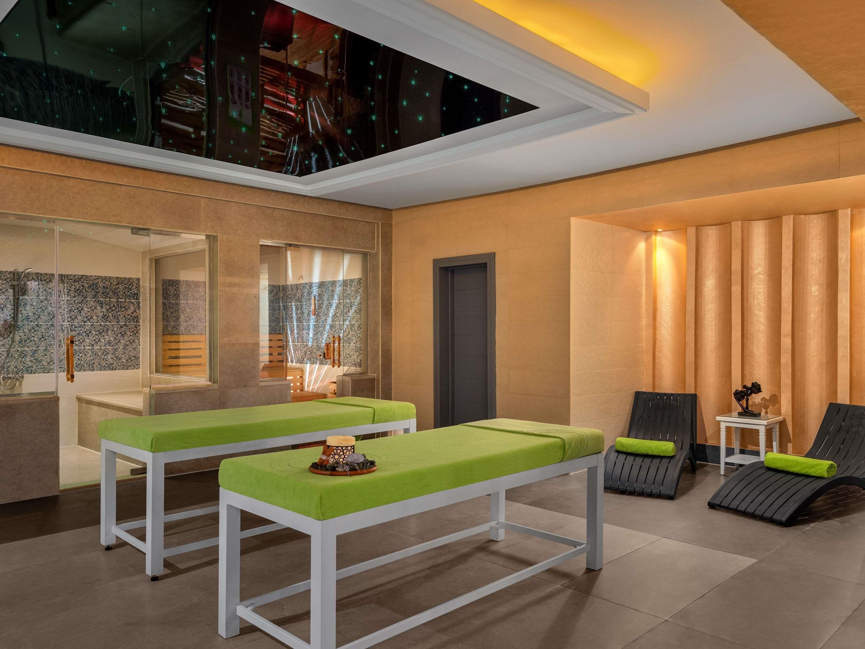 A modern spa room with two massage tables, a relaxation area with chairs, and a large skylight.