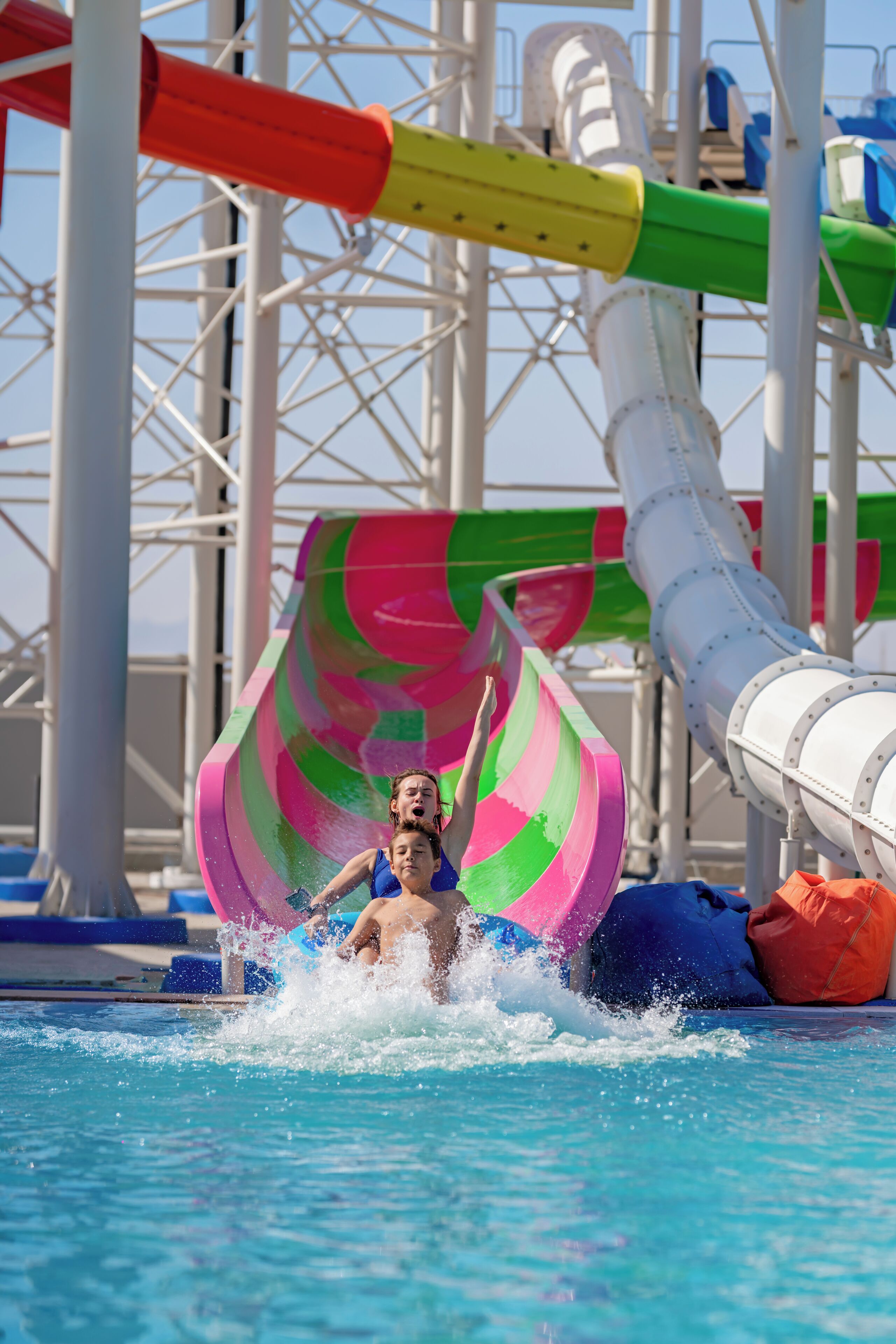 Un toboggan aquatique aux motifs en spirale et aux couleurs vives, une piscine et une structure métallique en arrière-plan.