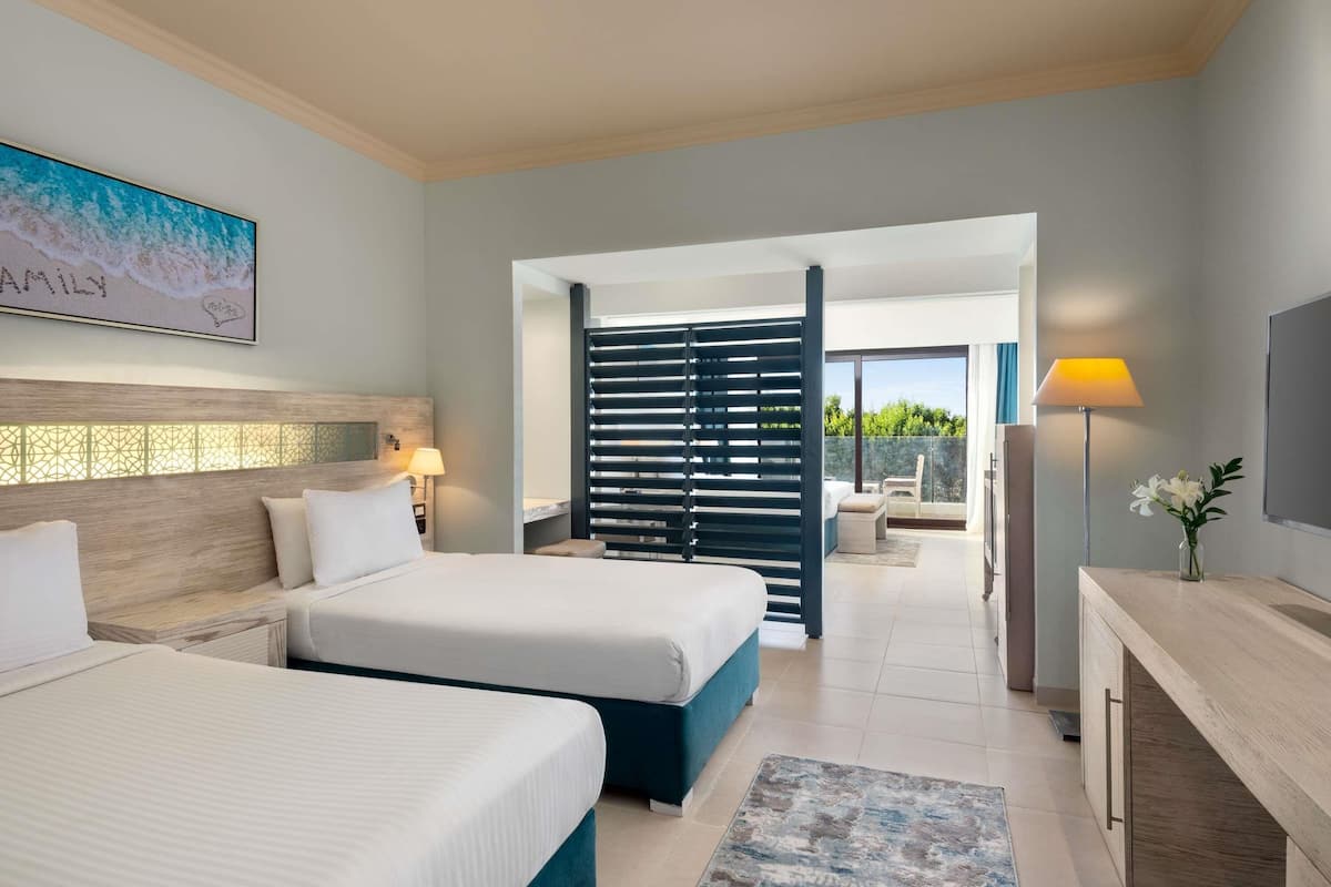 Habitación de hotel con dos camas, un escritorio, un televisor y un balcón con vistas.