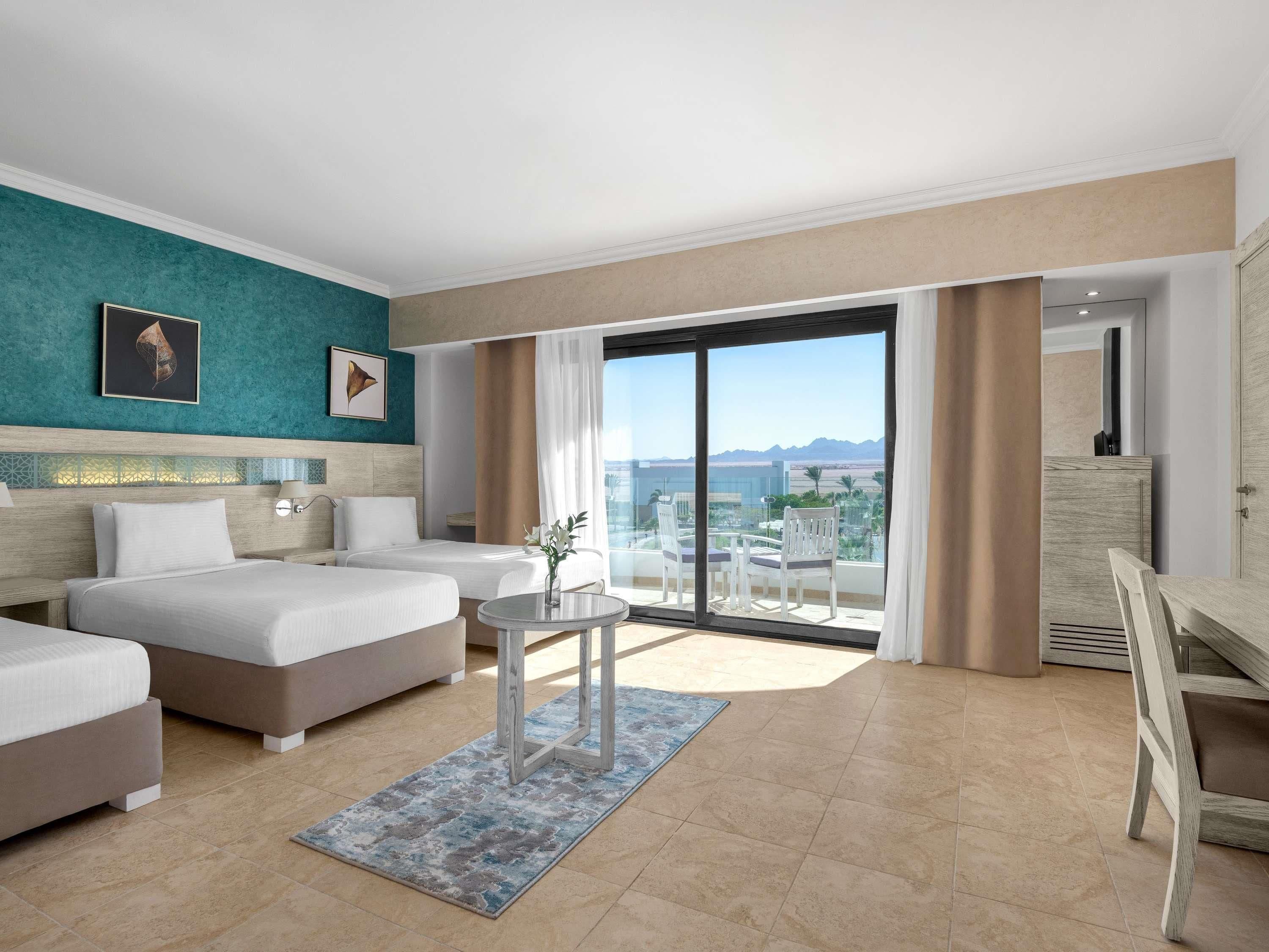 A hotel room with two beds, a balcony with a view, and a dining area.