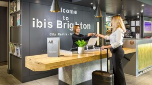 A reception desk at ibis Brighton City Centre with a modern design, a laptop, a plant, and a sign welcoming guests.