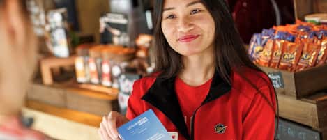 A person holding a brochure in a room with a wooden counter displaying snacks and a coffee machine.