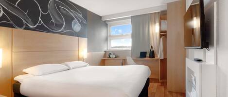 A modern hotel room with a large bed, a desk with a laptop, a flat-screen TV, and a window with a city view.