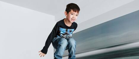A child jumping off a bunk bed in a modern room with white walls and a minimalist design.