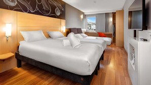 A hotel room with three beds, a wooden headboard, a large flat-screen TV, and a city view.