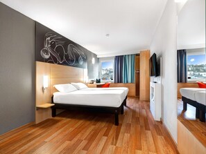 Une chambre d’hôtel moderne équipée d’un lit, d’un bureau, d’une chaise, d’une télévision et d’une fenêtre donnant sur la ville.