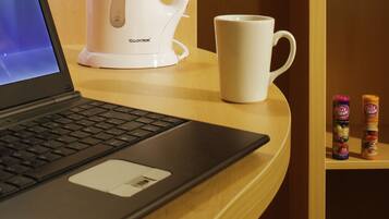 A laptop on a wooden table with a white coffee maker and a white mug beside it.