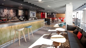 A modern bar area with a counter, stools, and a seating area with tables and chairs.