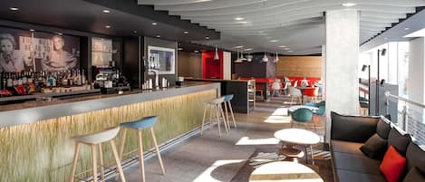 Zona de bar moderna amb barra, tamborets i seients amb taules i cadires.