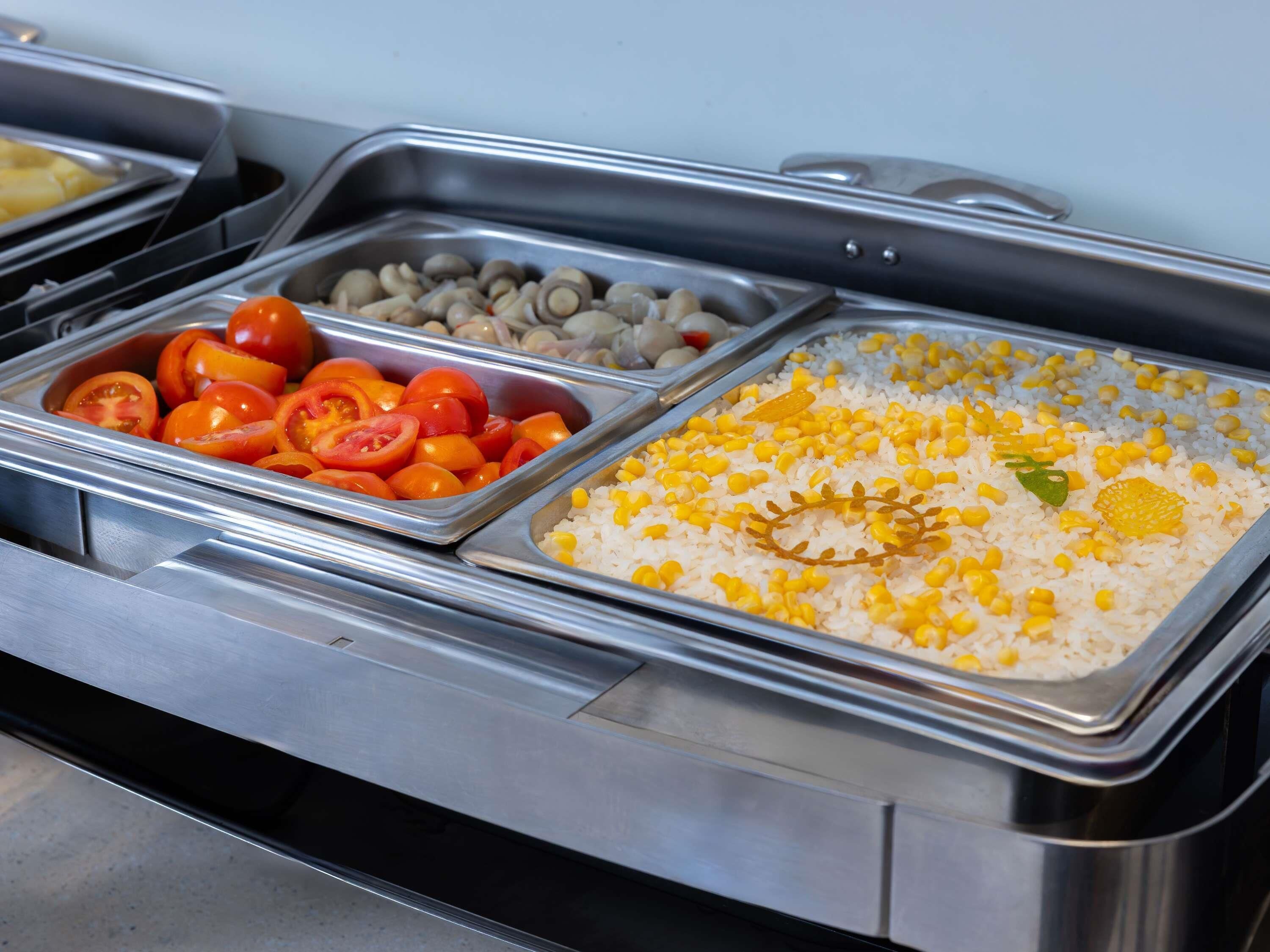 A buffet with various food options including tomatoes, corn, and rice.
