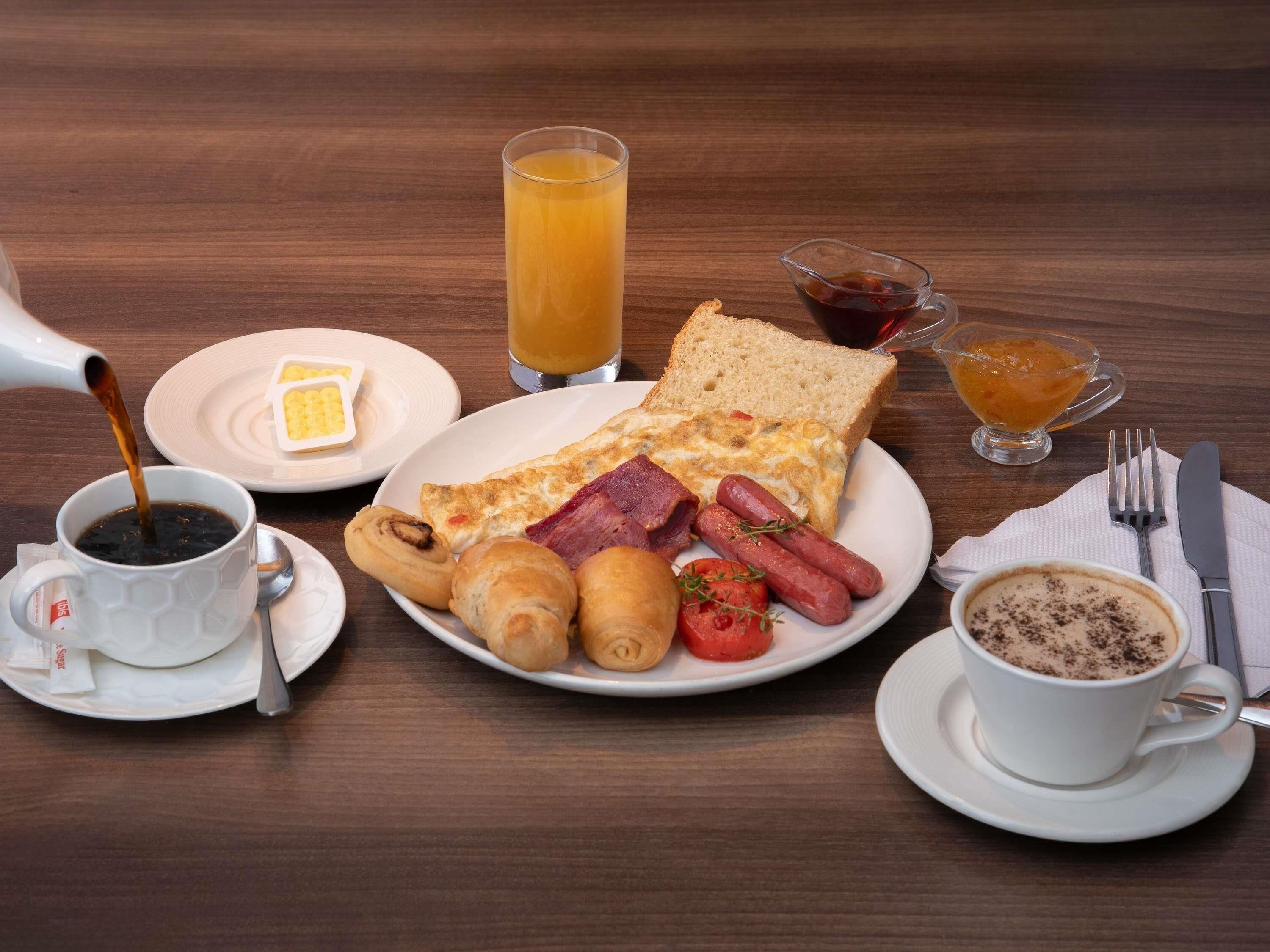 Un desayuno con diversas opciones de comida, como tostadas, huevos, salchichas y bollería, además de bebidas y salsas.
