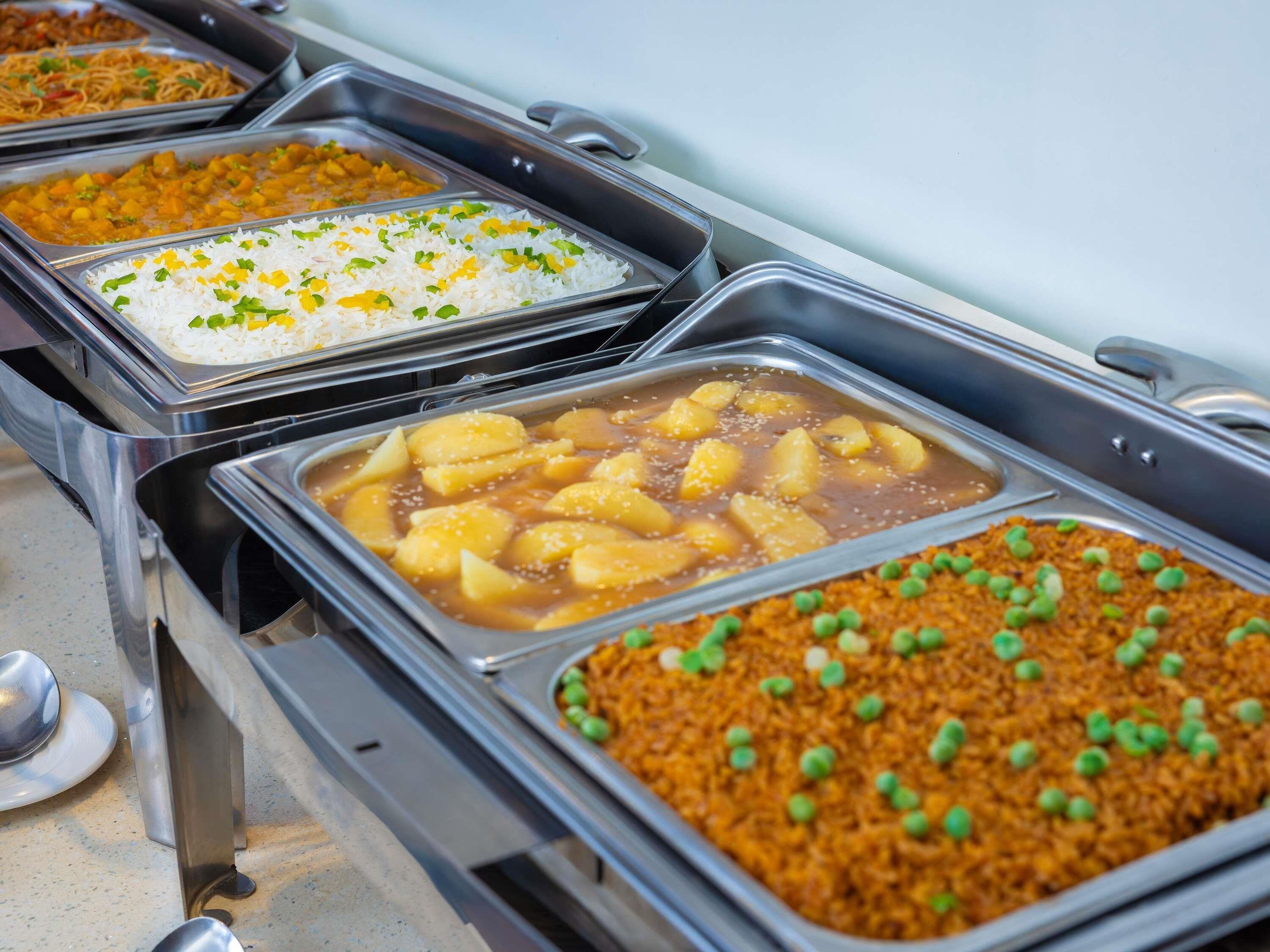 A buffet with various dishes including rice, a curry with potatoes, and a rice dish with peas.