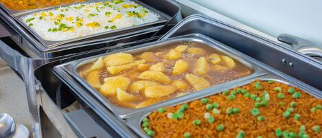 Un bufé con diversos platos, incluyendo arroz, un curry de papas y un plato de arroz con guisantes.