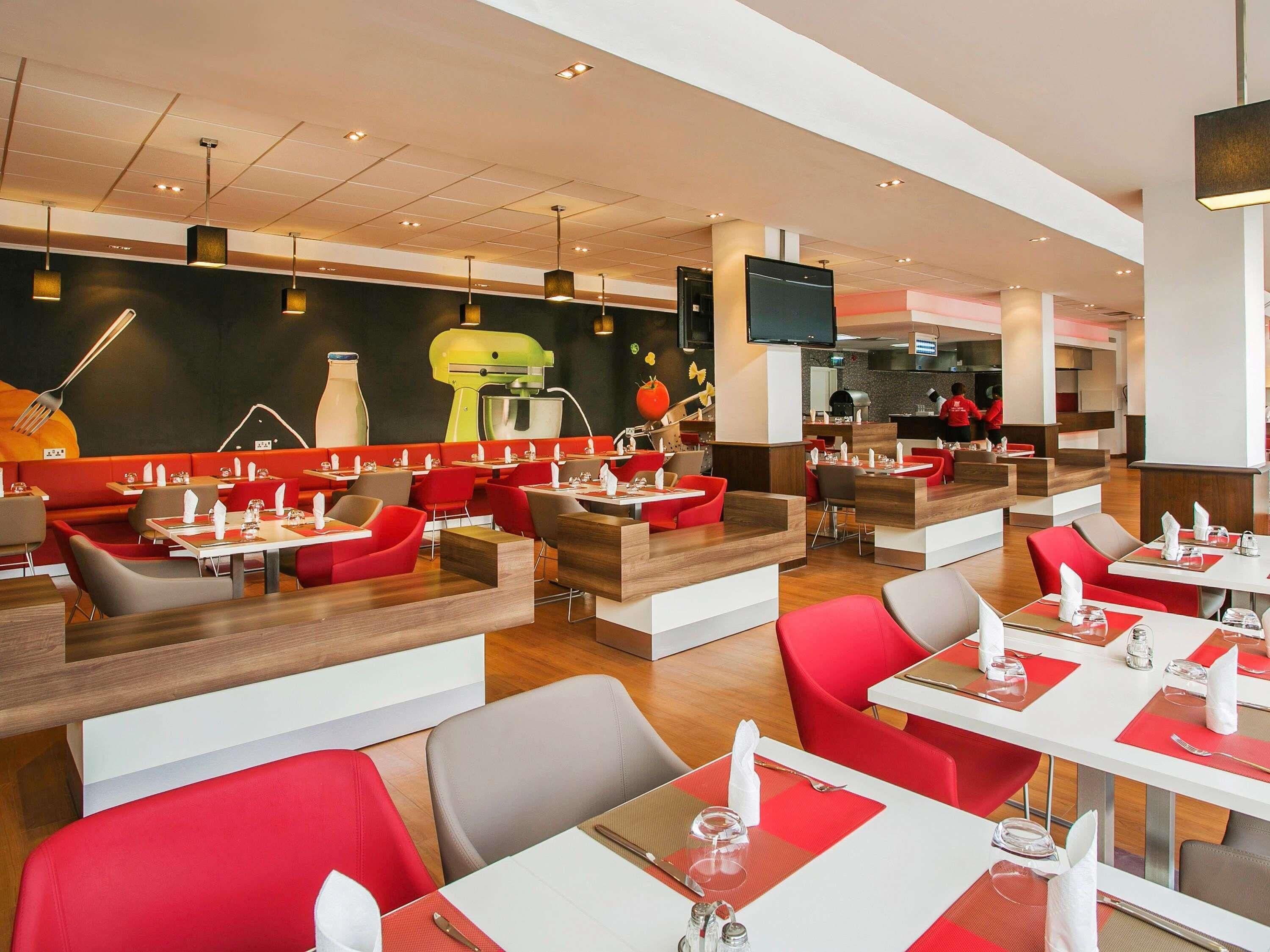 A modern restaurant interior with booths and tables, a kitchen area, and a flat-screen TV.