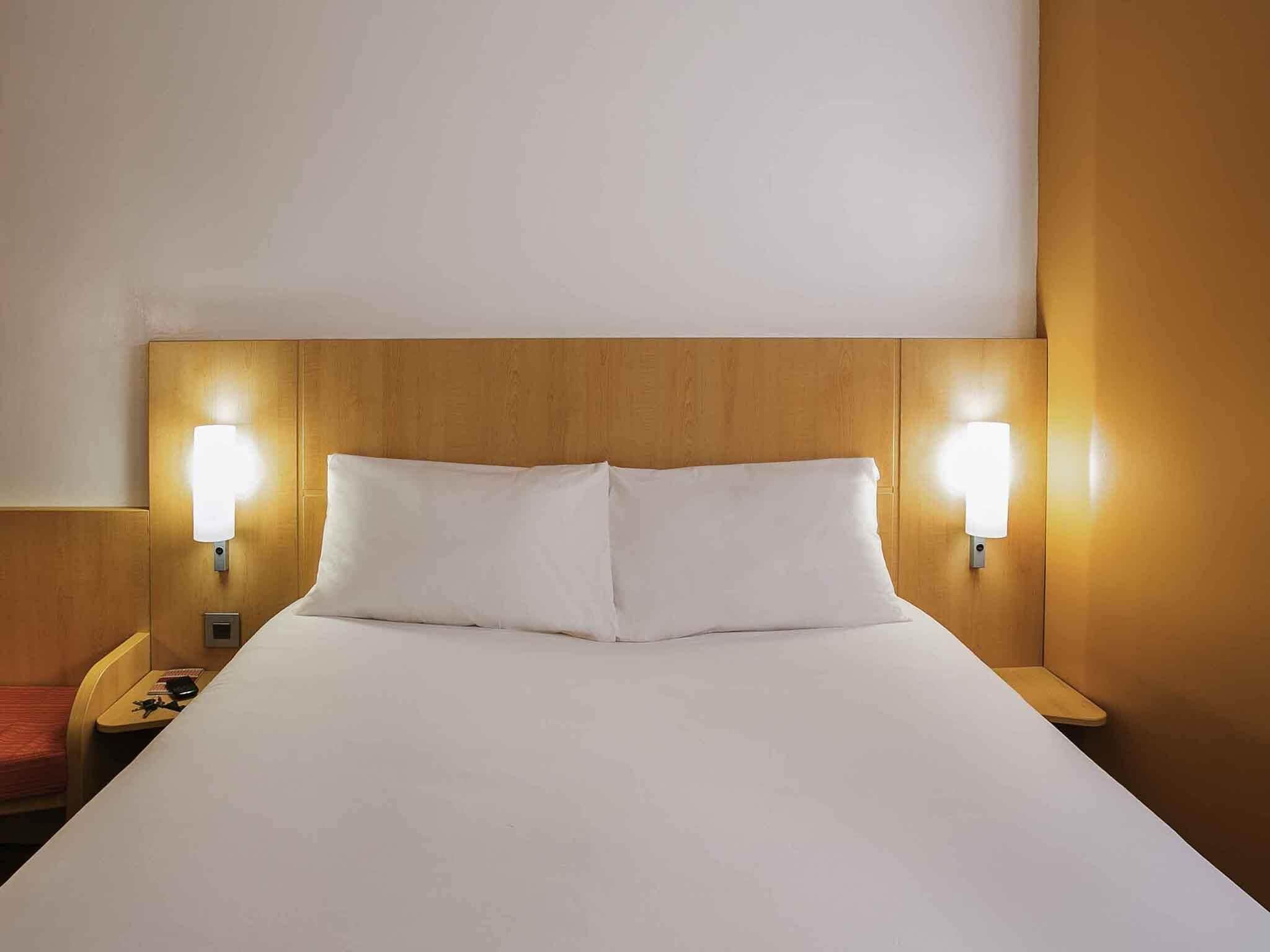 A hotel room with a large bed, two bedside lamps, and a wooden headboard.