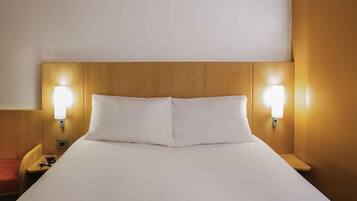 A hotel room with a large bed, two bedside lamps, and a wooden headboard.