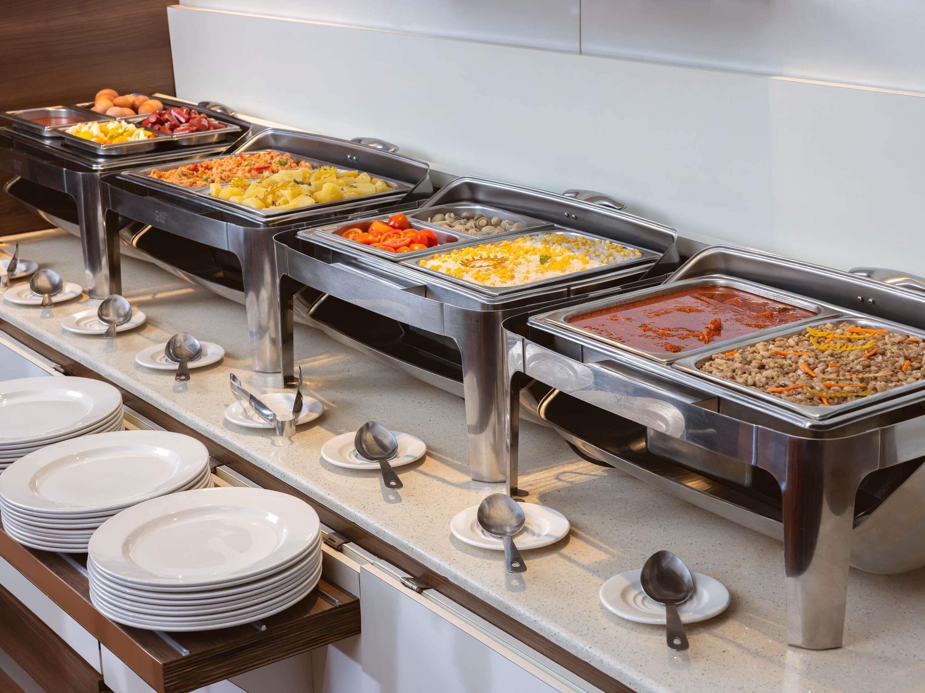 A buffet setup with various food items in trays, plates, and serving spoons.
