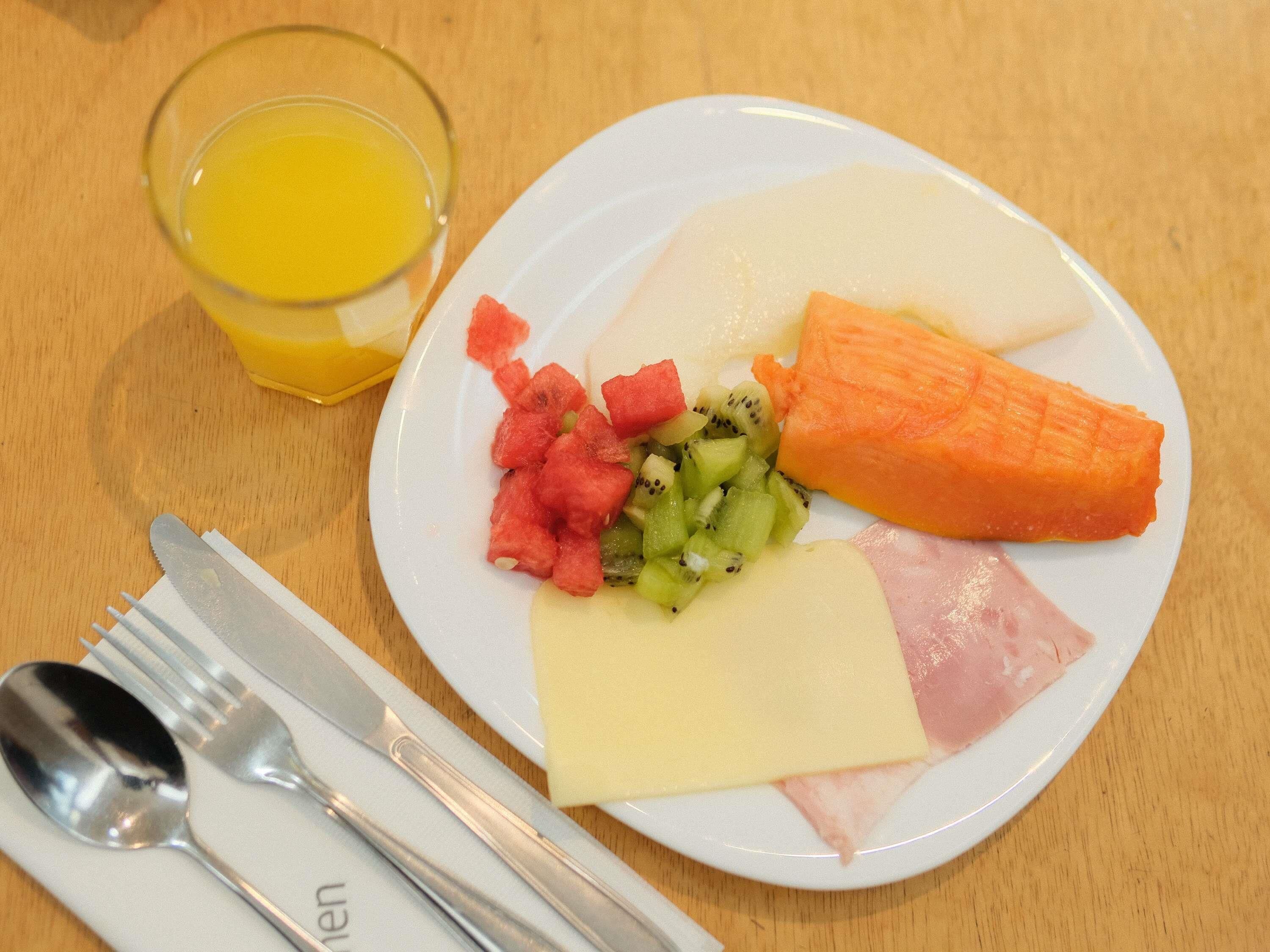 Une assiette remplie de divers fruits et un verre de jus d’orange sur une table en bois.