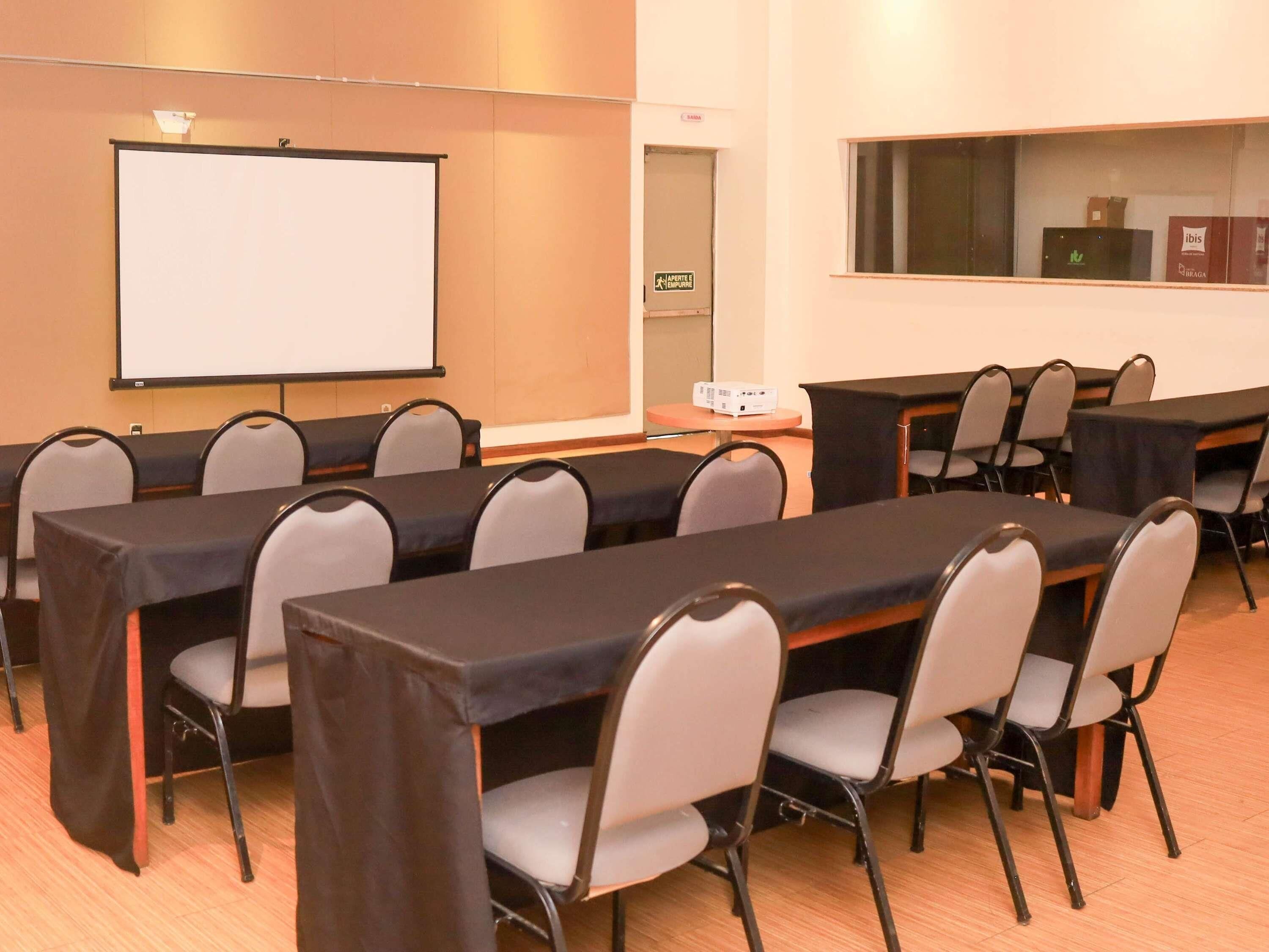 Una sala de conferencias con mesas, sillas, una pantalla de proyector y una puerta con un cartel.
