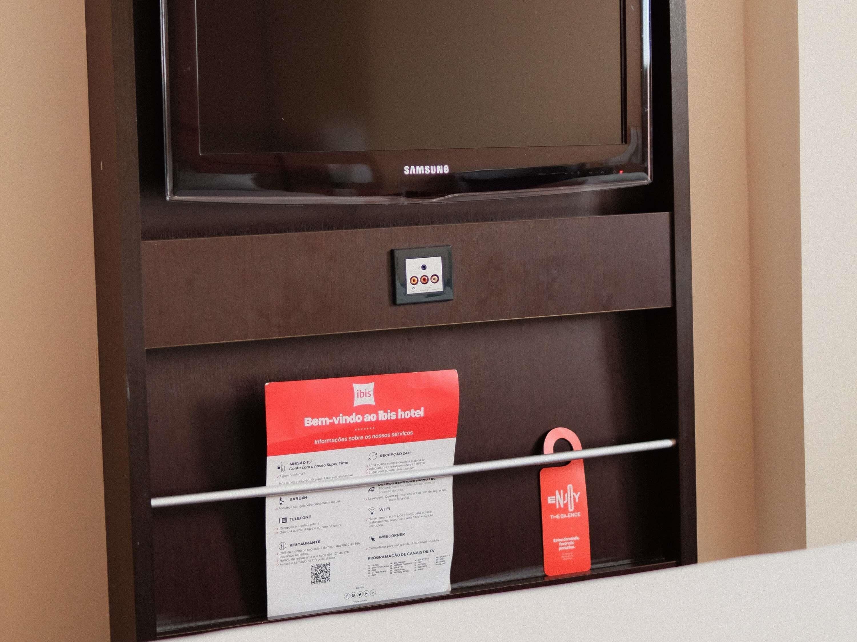 A hotel minibar with a Samsung TV, a minibar card, and a red tag.