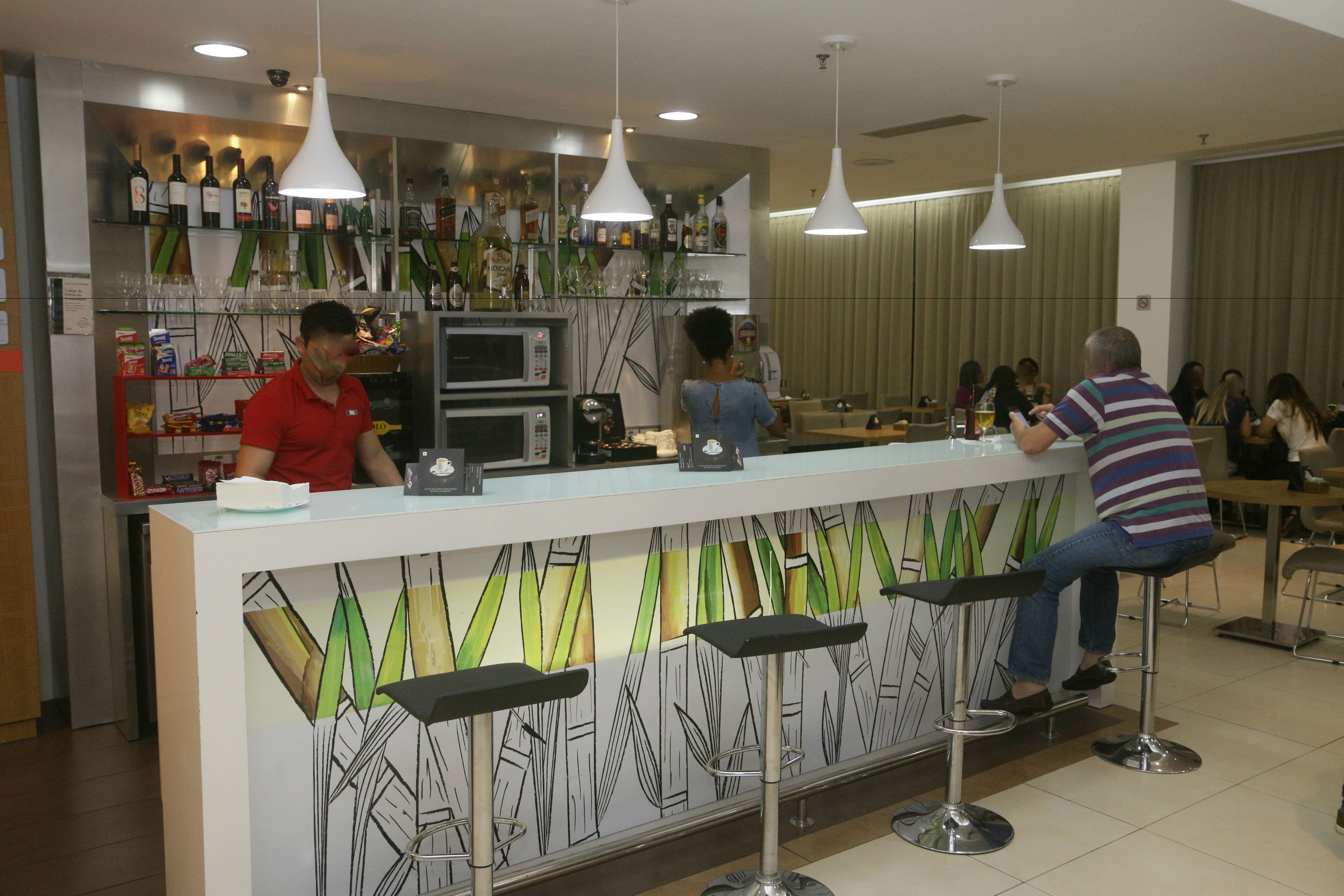 Zona de bar con mostrador, taburetes y una variedad de botellas y vasos en estantes.