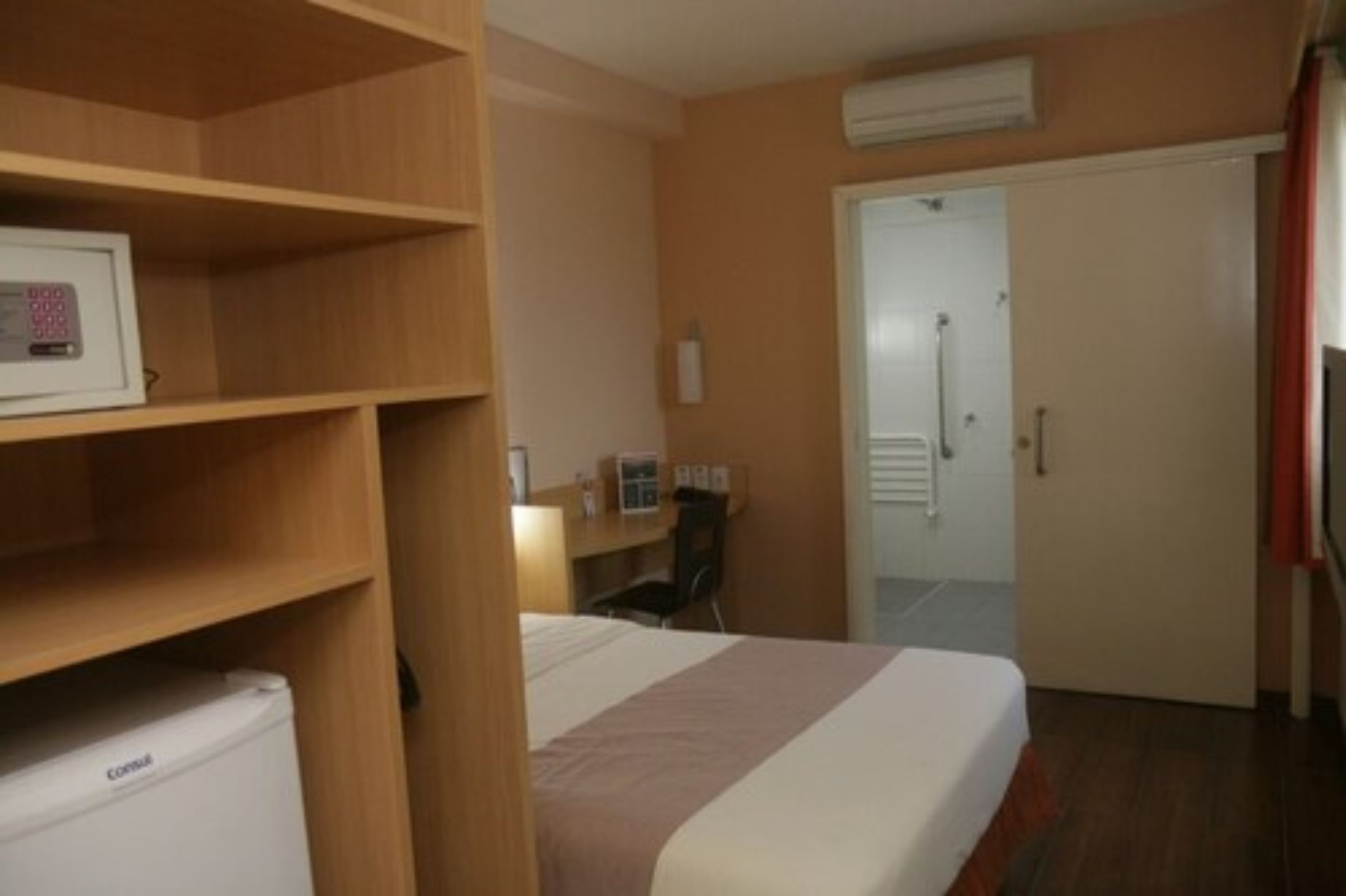 Habitación de hotel con cama, escritorio, silla, armario y puerta que da a un baño.