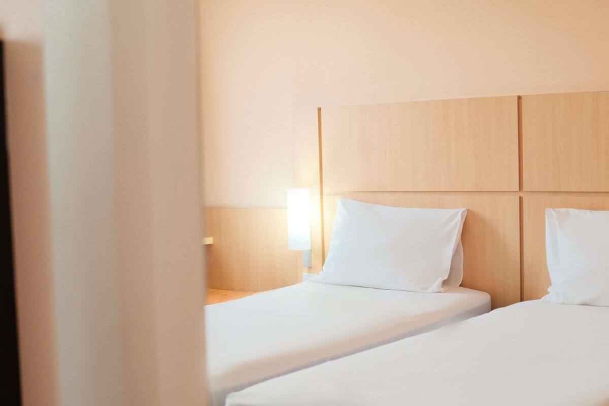 A hotel room with two single beds, a wooden headboard, and a bedside table with a lamp.