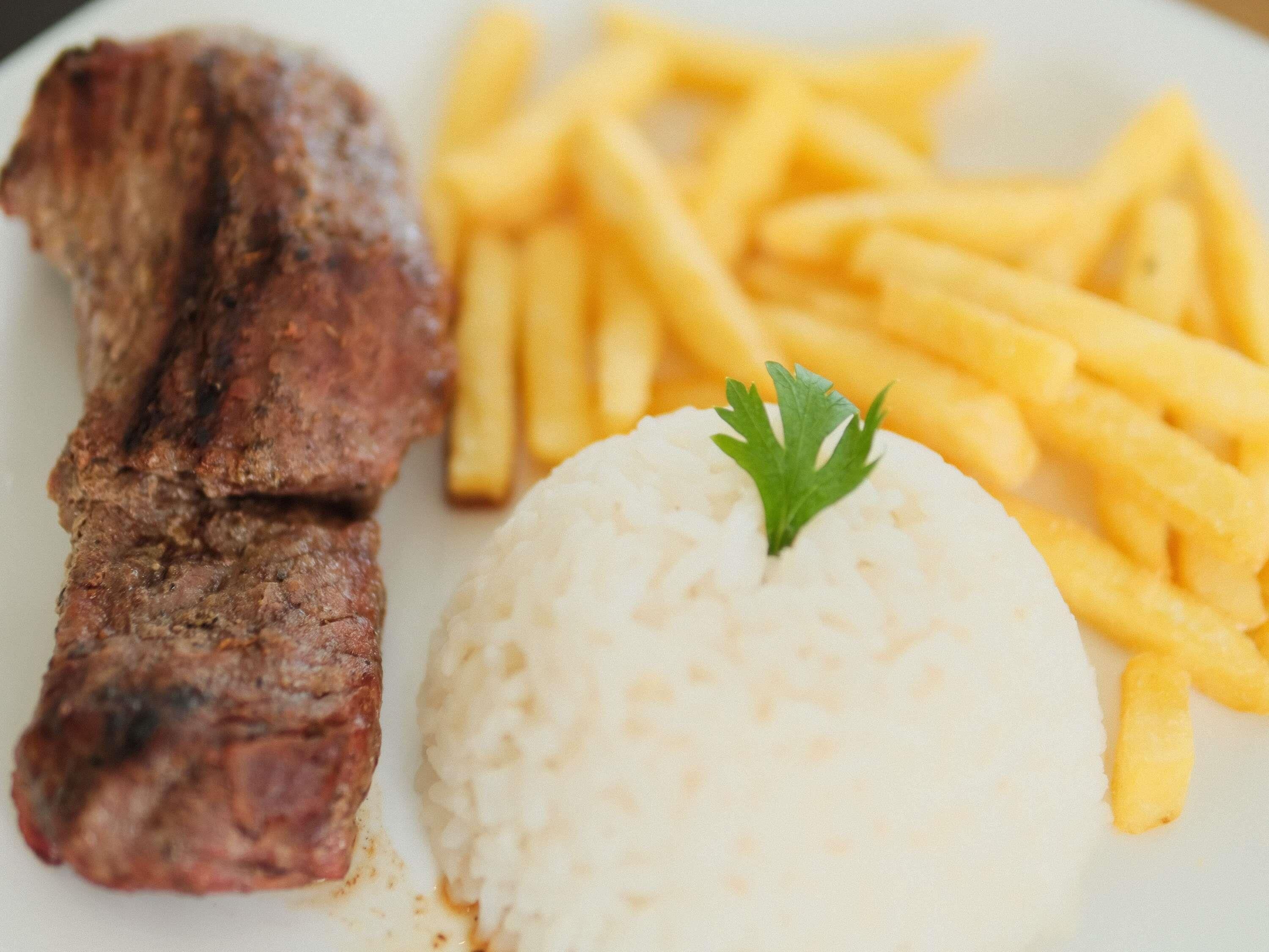 Un plato con un trozo de carne a la parrilla, papas fritas y una porción de arroz coronada con una ramita de perejil.